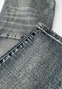 Blauwe denimstof met een vervaagde wasbehandeling, zichtbare stiksels en een gladde textuur met lichte variaties in kleur en patroon.