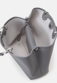 Szara skórzana torba typu tote o gładkiej fakturze, z przestronnym wnętrzem i zapinaną na zamek kieszenią, zabezpieczona srebrnym metalowym okuciem.