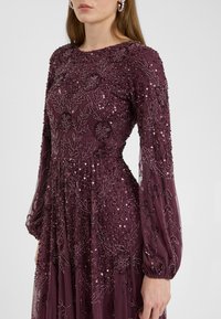 Abito lungo a maniche lunghe, color bordeaux, con ricami floreali intricati e paillettes. Gonna fluida con design a pieghe, in un tessuto morbido e strutturato.