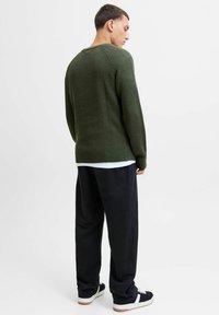 Donkergroene geribbelde trui met een ronde hals, gedragen met losse, donkere broek en zwarte sneakers. Gestructureerde stof, casual pasvorm.