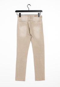 Vaqueros skinny beige colgados de un gancho negro. Incluye dos bolsillos traseros, una textura suave y una apariencia ligeramente desgastada.