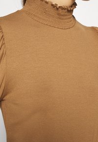 Brauner gestrickter Oberteil mit einem hohen, rüschigen Kragen, tailliertem Design und subtiler Textur. Verfügt über geraffte Details an den Schulternähten.