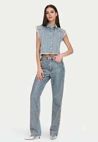 Gilet in denim corto con colletto, bordi sfrangiati e bottoni argentati, abbinato a jeans a vita alta e gamba dritta. Colore azzurro chiaro, motivo minimale.