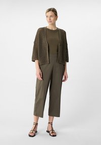 Oliwkowe, krótkie spodnie w połączeniu z teksturowanym, otwartym swetrem w brązowym kolorze oraz dopasowaną bluzką. Całość dopełniają czarne sandały na paski.