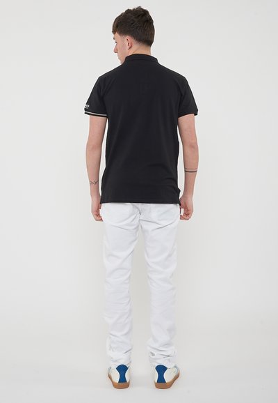 Polo nero con maniche corte, pantaloni bianchi e sneakers con accenti blu. Il polo presenta un colletto e un sottile dettaglio a righe.