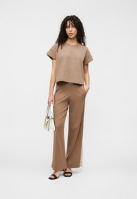 Καφέ κοντό t-shirt με υφή και κοντά μανίκια, συνδυασμένο με καφέ παντελόνια φαρδιάς γραμμής με πλαϊνές σχισμές και διακριτική ετικέτα.