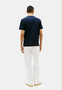 Maglietta in cotone blu navy con collo a giro, maniche corte e taglio dritto, abbinata a pantaloni bianchi e sneakers chiare.