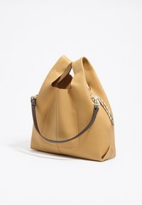 Borsa a tracolla gialla in pelle con una texture morbida, una forma curva unica, tracolla intrecciata e design con apertura superiore.