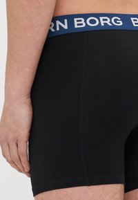 Schwarze Boxershorts mit einem breiten marineblauen Bund, auf dem weiße "BORG"-Buchstaben prangen. Der Stoff wirkt glatt und hat eine enganliegende Passform.