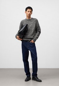 Szary sweter z teksturowanym splotem, niebieskie dżinsy, czarne skórzane buty i czarna torebka, na jednolitym białym tle.