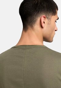 Tricou verde olive cu mâneci scurte, având un guler rotund și cusături vizibile. Textură netedă și design simplu.