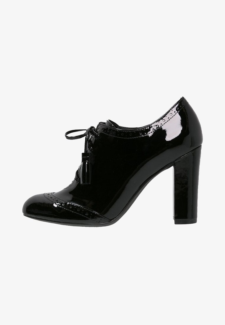 Chaussure derby pour femme en cuir verni noir avec talon bloc, lacets à glands et détails brogués sur le bout et les bords supérieurs.