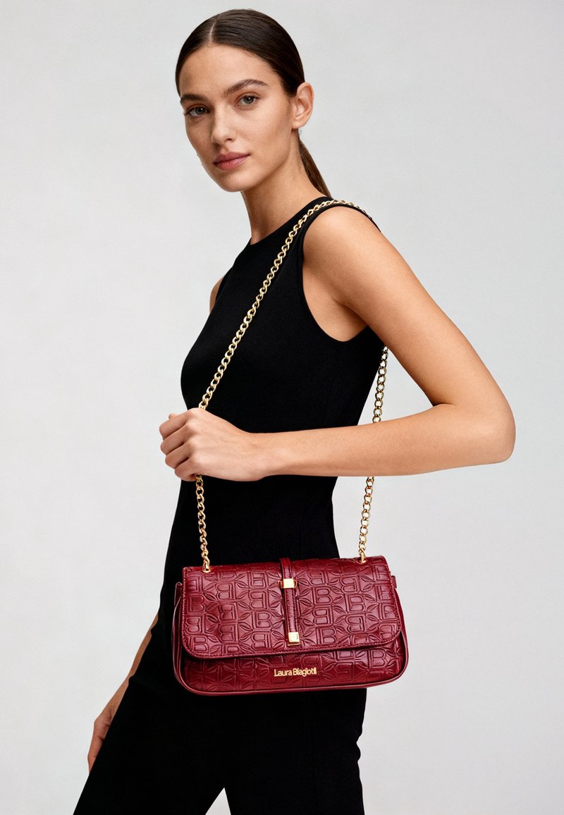 Borsa a tracolla bordeaux con finitura testurizzata, tracolla a catena dorata e dettagli con logo. Forma rettangolare con design a patta pieghevole.