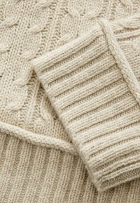 Beige Strickpullover mit Kabel- und Rippstrickmustern, aus dickem Wollmaterial, mit einer weichen Textur und sichtbaren Nähten.