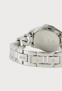 Silver stainless steel watch with a link bracelet, featuring engraved "GUESS" logo and a round case with a screw-down crown.