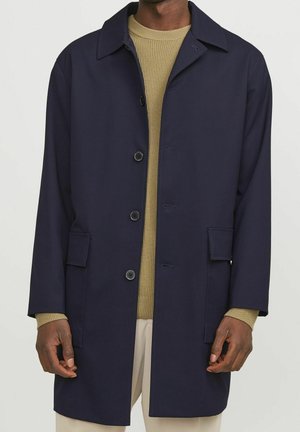 Navy trenchcoat met kraag, sluiting met knopen aan de voorkant, twee zijzakken en een rechte snit. Gelaagd over een gestructureerde beige trui.