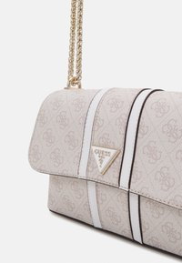 Beige käsilaukku, jossa on teksturoitu kangas, kultaketjuhihna, valkoiset raidat ja kolmion muotoinen logolevy edessä.