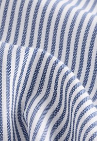 Tissu tissé rayé bleu et blanc avec un motif texturé et des plis doux créant une apparence ondulée.