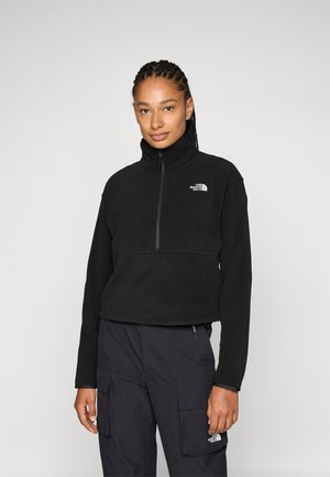 Black fleece pullover with high collar and half zipper, featuring a chest logo. Paired with dark cargo pants, smooth texture.