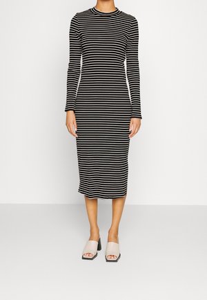 Abito a strisce in bianco e nero, maniche lunghe, scollatura alta, lunghezza midi, design aderente. Indossato con sandali con tacco a blocco grigio chiaro.