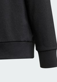 Sudadera negra con puños y dobladillo acanalados, hecha de una tela texturizada, con un diseño limpio y una silueta ajustada.