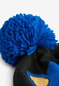 Schwarze Strickmütze mit einem großen blauen Pompon oben. Hat ein farbenfrohes Design mit blauen und gelben Akzenten. Weicher Stoff, gemütliches Aussehen.