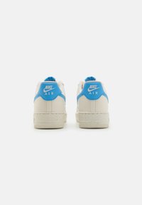 Reebok Air tenisky v krémové a modré barvě, s hladkým koženým svrškem, gumovou podrážkou a vyraženým logem na patě. Přítomné texturované akcenty.
