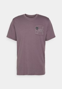 Camiseta de cuello redondo de manga corta en color púrpura con un bolsillo en el pecho que presenta un gran logotipo contorneado y una pequeña etiqueta de la marca en negro.