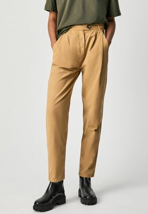 Pantaloni beige realizzati in tessuto morbido, caratterizzati da un vita alta, una parte anteriore plissettata, tasche laterali e una chiusura con bottone, abbinati a stivaletti neri alla caviglia.