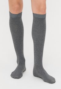 Calze grigie al ginocchio con texture a coste, caratterizzate da una finitura morbida e un risvolto in contrasto. Il tessuto sembra leggero ed elastico.