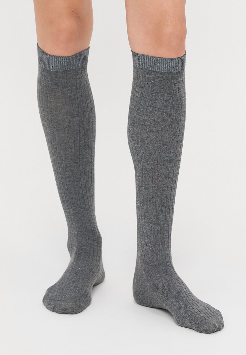 Calze grigie al ginocchio con texture a coste, caratterizzate da una finitura morbida e un risvolto in contrasto. Il tessuto sembra leggero ed elastico.