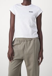 Bílý krátký rukáv tričko s černým obdélníkovým logem Levi's na levé hrudi, doplněné světlými olivovými kalhotami v uvolněném střihu.