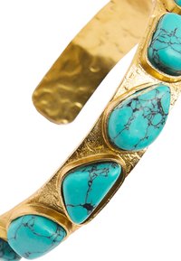 Złota bransoletka na nadgarstek z pięcioma nieregularnie ukształtowanymi kamieniami turkusowymi z czarnymi żyłkami, osadzona w fakturowanej złotej obręczy.