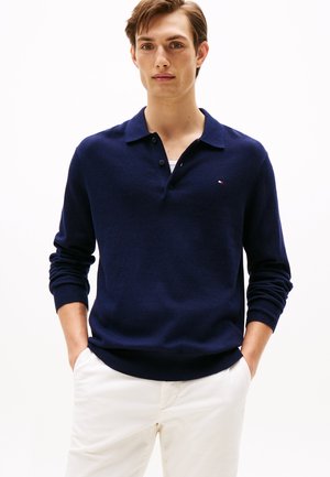 Marineblauwe gebreide polo trui met een drieknopenpailletten en geribbelde manchetten. Witte accentlogo op de borst. Draag met lichtgekleurde broeken.