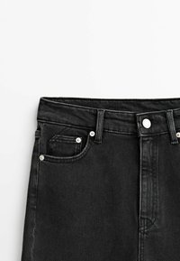 Détail de la taille d'un jean en denim noir, avec bouton, passants de ceinture et poches avant sur fond blanc.