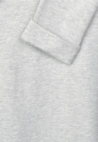 Světle šedá pletenina s jemnou strukturou, s přehnutým okrajem rukávu a jemnou variací v odstínech.