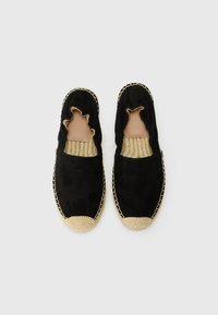 Espadrilles en daim noir avec un bord festonné, une semelle en corde tressée et une bordure en jute beige autour de l'orteil. Doublure intérieure lisse visible.