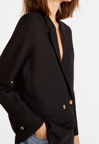 Blazer in lino nero con colletto a sciallata, chiusura a doppio bottone e bottoni marroni. Presenta una vestibilità slim e maniche lunghe.