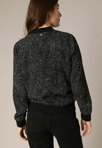 Zwarte trui met een textuurpatroon van witte wervelingen, ribgebreide boorden en zoom, relaxte pasvorm en een ronde halslijn. Zicht van achteren.