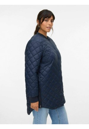 Manteau long matelassé marine avec un col rond, des boutons pression, des zips sur les côtés et des poignets côtelés pour une texture et une dimension supplémentaires.