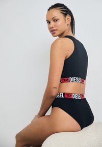 Ensemble de brassière de sport noire et de culotte taille haute, avec une bande logo Diesel rouge et blanche audacieuse. Texture lisse avec une coupe ajustée.