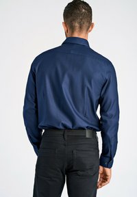 Donkerblauwe shirt met lange mouwen van textuurstof, met een gebogen zoom en knoops mouwen, gecombineerd met zwarte broeken met achterzakken.