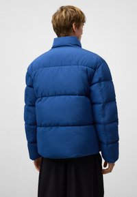 Niebieska kurtka puffer z pikowanym wzorem, wysokim kołnierzem i gładką fakturą. Widoczne szwy i puszyste wypełnienie dla zapewnienia ciepła.