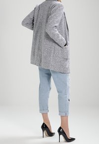 Šedý texturovaný dlouhý kabát s kapsami, zkombinovaný se světle modrými opranými sukni s rolovanými nohavicemi a černými lodičkami.