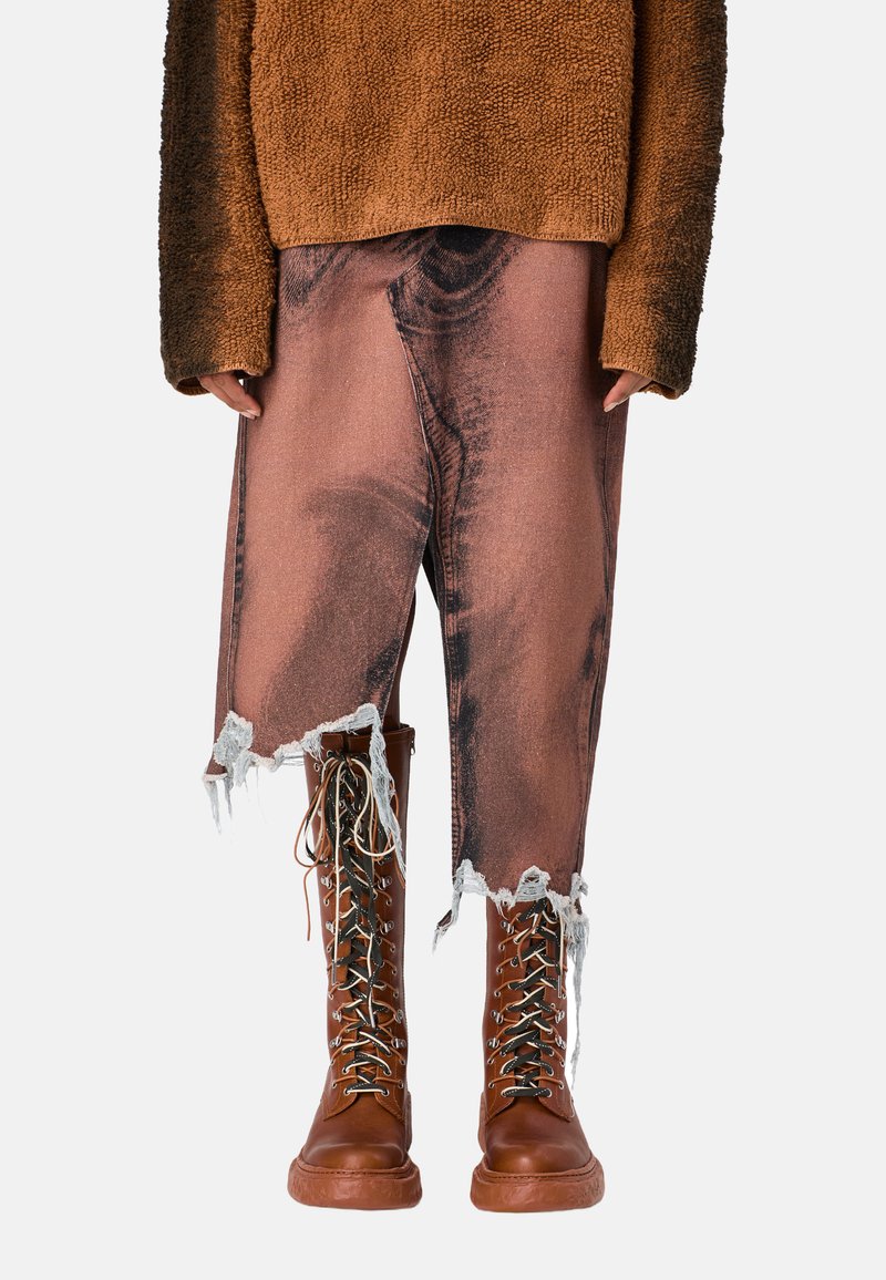 Brązowy sweter o fakturze, zniszczone różowe dżinsy z postrzępionym dołem oraz brązowe lace-up buty wojskowe z akcentami ze srebrnego hardware'u.