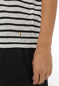 Stribet kortærmet top i lys grå og sort med en guld logoaccent nær nederste kant. Stoffet ser letvægts og åndbart ud.