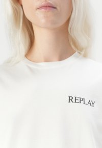 Witte katoen t-shirt met korte mouwen, voorzien van een zwart "REPLAY" logo aan de linkerkant. Gladde textuur en ronde halsontwerp.