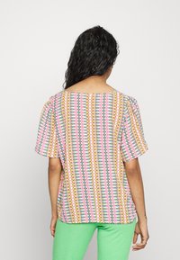Top de manga curta com um padrão multicolorido geométrico, apresentando tons de rosa, amarelo e azul, com um decote amplo e detalhe de ombro franzido.