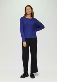Blauer gerippter Strickpullover mit langen Ärmeln, runder Ausschnitt, kombiniert mit schwarzen, weiten Hosen und glänzenden schwarzen Schuhen. Schlichtes, strukturiertes Design.