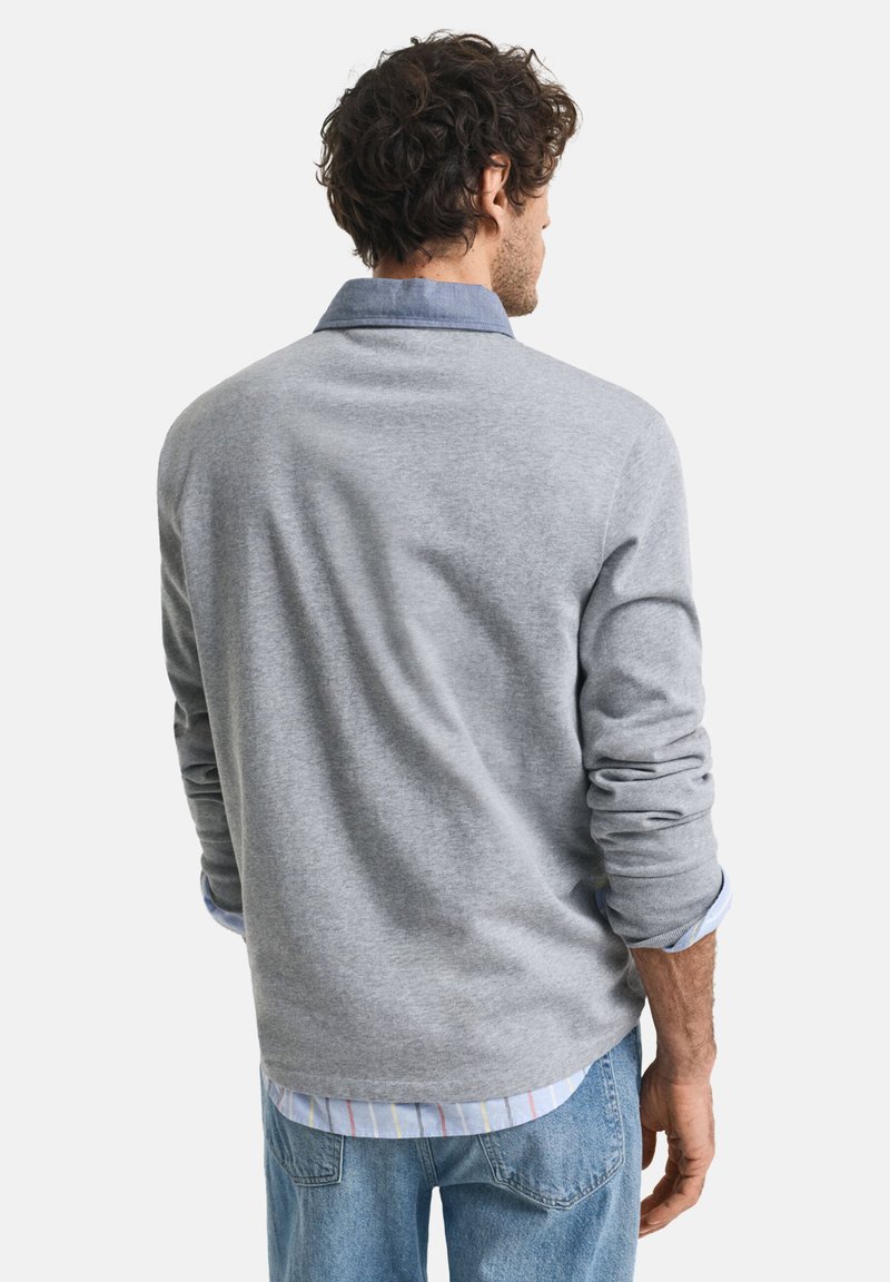 Jersey gris con una textura suave, que presenta un cuello azul y puños enrollados sobre una camisa de rayas. Modelo mostrado de espaldas.